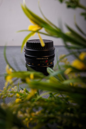 Izmail, Ukraine. April 2022. USSR Helios lens for photo camera on grey background with yellow flowers. Old photo equipment, lens brandのeditorial素材
