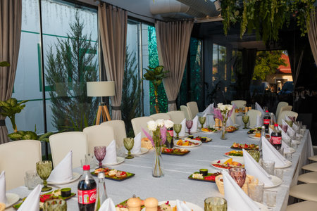 Izmail, Ukraine. October 2021. Festive table with appetizers. Salads, cheese and meat plates. Empty glasses, plates, chairs for guests in restaurantのeditorial素材