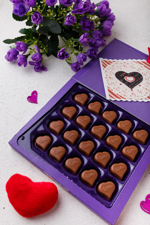 Izmail, Ukraine. 14 February 2022. Violet box of heart shaped chocolates Milka, flowers, postcard on white. Valentines day sweetsのeditorial素材