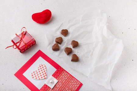 Izmail, Ukraine. 14 February 2022. Heart shaped chocolates Milka, fabric heart toy, candle and postcard on white paper. Valentines day sweetsのeditorial素材