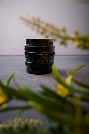 Izmail, Ukraine. April 2022. USSR Helios lens for photo camera on grey background with yellow flowers. Old photo equipment, lens brandのeditorial素材