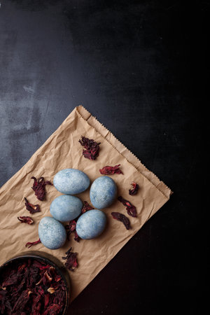 Beautiful DIY painted Easter eggs, dry Hibiscus tea in black bowl. Easter black wooden background. Top view, copy space, vertical shotの写真素材