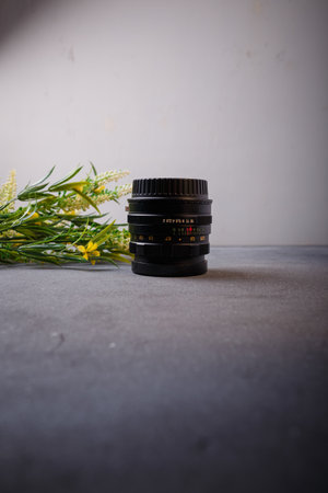 Izmail, Ukraine. April 2022. USSR Helios lens for photo camera on grey background with yellow flowers. Old photo equipment, lens brandのeditorial素材