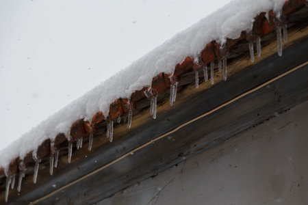transparent icicles hanging from roof at cold winter day, weather concept