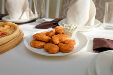 Crisp chicken nuggets and cheese sauce on white plate. FEstive table in restaurant for children,...