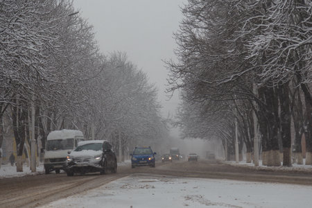 Izmail, Ukraine. February 2022. Winter city landscape, cars driving the road, trees covered with snow, snowfall weatherのeditorial素材