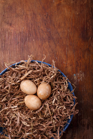 Plate decorated as bird nest with brown colored eggs on rustic background. Happy Easter. Top view, copy space, vertical shotの写真素材