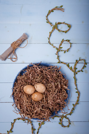 Plate decorated as bird nest with brown colored eggs on blue background. Happy Easter. Top view, copy space, vertical shotの写真素材