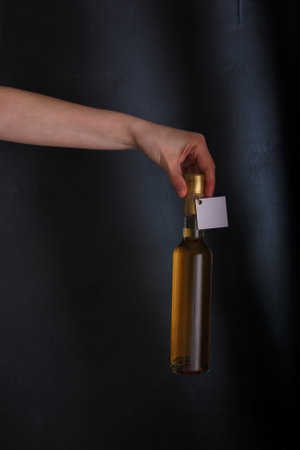 Hand holding bottle of white wine with template label, no brand. Riesling, chardonnay, sauvignon blanc. Alcohol beverage on black backgroundの写真素材