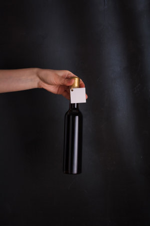 hands holding 250 ml bottle of red wine with mock up label, no brand on black background. Cabernet sauvignon, merlot, pinot noir. Alcohol drink, copy spaceの写真素材