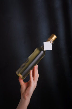 female hand holding 250 ml bottle of white wine with mock up label, no brand on black background. Alcohol drink, copy spaceの写真素材