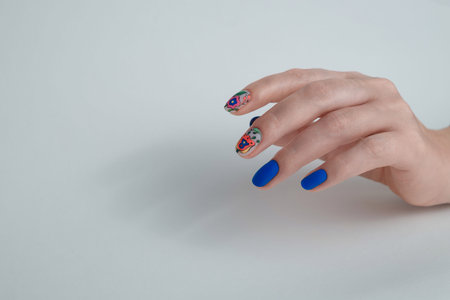 Beauty service. Female hand with blue manicured nails and flowers design. Gel varnish nail art....