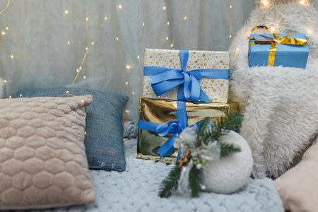 three wrapped Christmas presents on sofa with cushions, garland lights on background.の写真素材