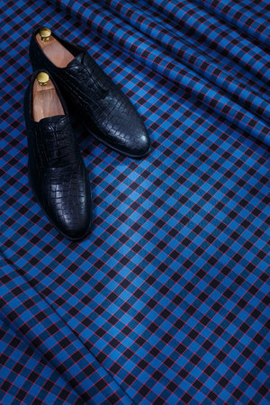 Male black leather shoes on dark blue checkered suit fabric background. Copy space for logo, design, advertising. Classic formal accessories for men.の写真素材