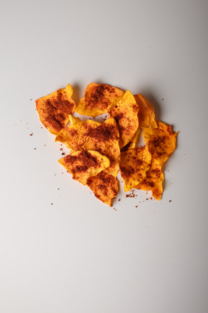 Heap of dried pumpkin slices, dry vegetable crisps, chips pile with pepper and paprika on white background. Advertising banner, copy space. Product presentation. Vertical shot.の写真素材