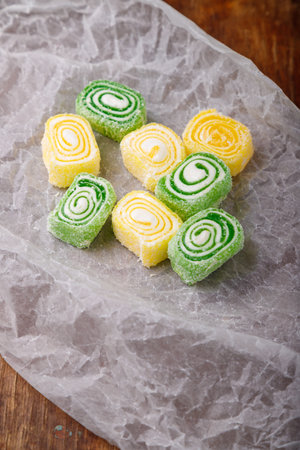 Turkish delight, yellow and green locum roll with coconut flakes on white paper, wooden background. Eastern sweets, oriental food. Traditional tasty dessert. Copy space. Top viewの写真素材