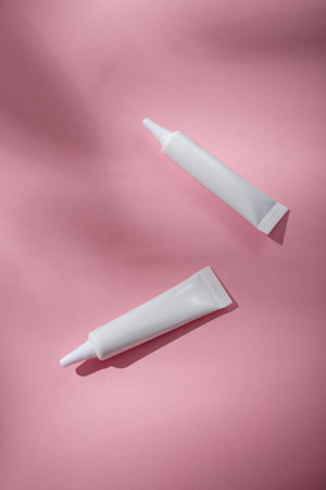 Two white narrow unbranded cosmetics tubes mockup on pink background. Beauty product template, advertising banner. Copy space, top view, flat lay.の写真素材