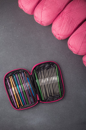 Crochet tools kit, set of crocheting hooks in a case. Organizer with equipment for creative handicraft. Some skins of bright pink yarn on background. Top view, copy space. Vertical shot.の写真素材