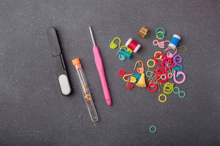 Crocheting tools kit. Set of crochet hook, thimble, pins, markers and other equipment for creative handicraft on gray background. Closeup, top view.の写真素材