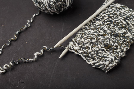 Melange gray white yarn balls on black background, close up shot. Knitting needles with part of knitwear. Starting of knitted cloth.の写真素材