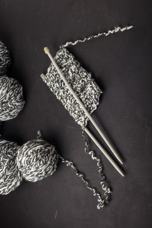 Melange gray white yarn balls on black background, close up shot. Knitting needles with part of...