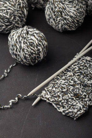 Melange gray white yarn balls on black background, close up shot. Knitting needles with part of knitwear.の写真素材