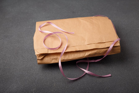 Brown paper package with pink ribbon on gray background. Present packaging, gift pack. Unbranded template, no label or logo. Copy space.の写真素材