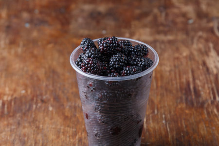 Ripe blackberries in plastic cup on brown old wooden rustic table background, close up shot.の写真素材
