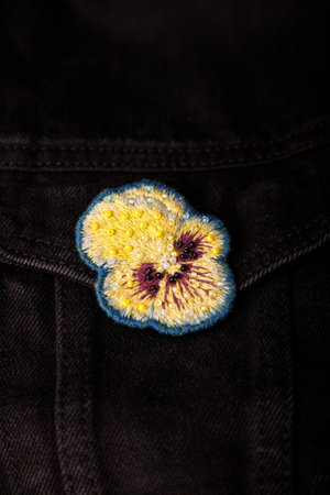Pansy, heartsease embroidery brooch with beads on black jeans fabric background, closeup shot, copy space.の写真素材