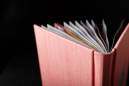 Half open photobook, photo album in pink leather cover on black background. Close up shot of book...