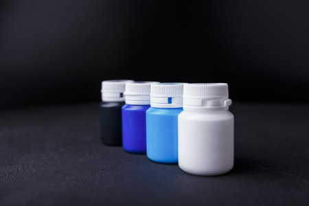 Small bottles of blue, white and black acrylic or gouache paint jars in a box on dark background....