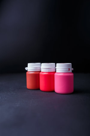 Small bottles of pink and red acrylic or gouache paint jars in a box on dark background....