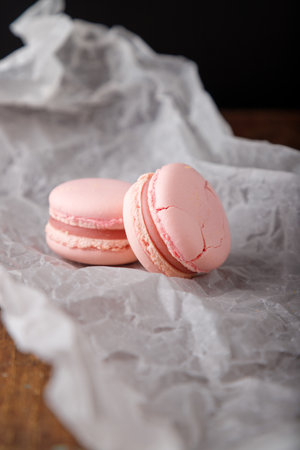 Tender pink macaroons on paper, wooden background. Forest berries, strawberry or raspberry flavor. Copy space.の写真素材