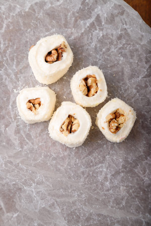 Turkish delight, white locum roll with walnut and coconut flakes on white paper, wooden background. Eastern sweets, oriental food. Traditional tasty dessert. Copy space. Top viewの写真素材