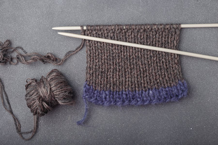 Knitting needles with part of knitted garment, mohair and acrylic yarn balls on gray background.