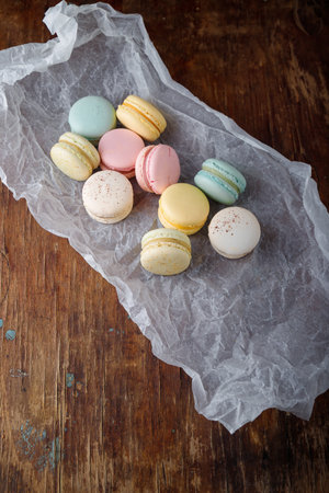 Tender multicolored macaroons with different flavors on paper, wooden rustic background. Top view, copy spaceの写真素材