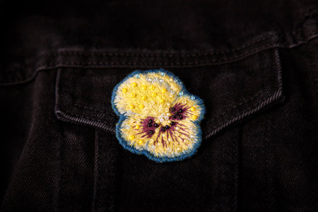Pansy, heartsease embroidery brooch with beads on black jeans fabric background, closeup shot, copy space.の写真素材