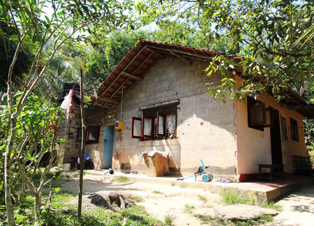 rustic countryside house built from bricks with a tiled roof, surrounded by lush greenery. The simple home has open windows and scattered household items, reflecting a peaceful rural lifestyleの写真素材