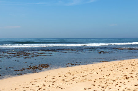 Seascape with waves rolling onto sandy shore on sunny day. Footprints in sand near waters edge. Natural seascape, shotsの写真素材
