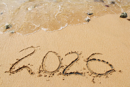 words 2026 and number written in sand on beach with waves on top. Happy New Year backgroundの写真素材