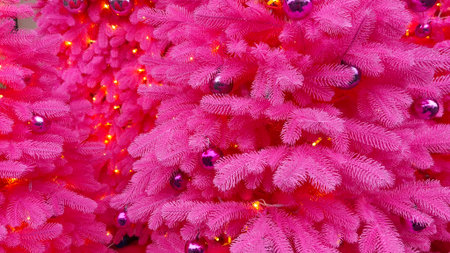 Vibrant pink Christmas tree branches decorated with shiny ornaments and warm lights, creating a bold and festive holiday background full of color and seasonal cheerの写真素材