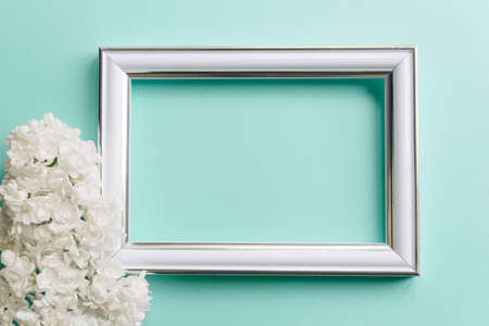 White photo frame and white flowers on mint background. Flat lay, top view.の写真素材