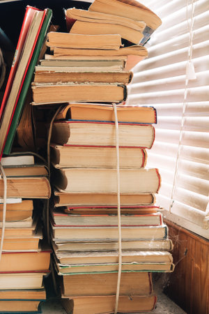 A stack of old books on a shelf in a room with blinds