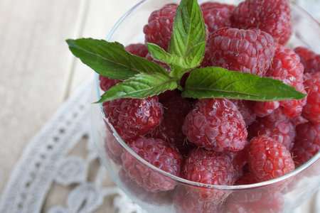 Red raspberries in white plate on beige wooden background. Large raspberriesの写真素材
