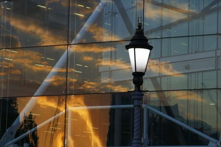 old lantern and abctract modern glass building with sunset sky reflectionの写真素材
