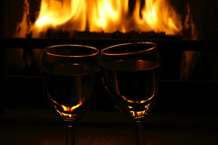 two wine glasses against fireplace with flame in dark lightの写真素材