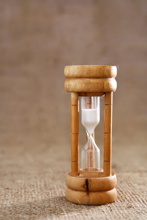An old wooden hourglass against a textured hessian background, shallow DOF