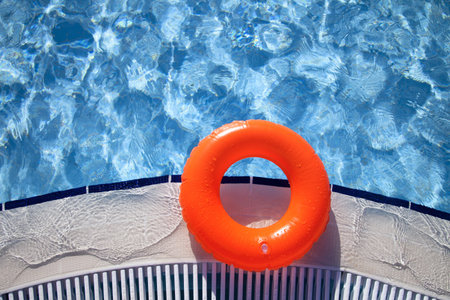 floating orange ring on edge of swimpool with waves reflecting in the summer sunの写真素材