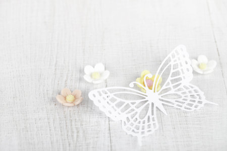 paper butterfly and three sugar blossom flowers on white old tableの写真素材