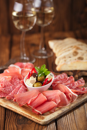 antipasti Platter of Cured Meat,   jamon, olives, sausage, salami,  ciabatta and white wine glasses on textured wooden tableの写真素材